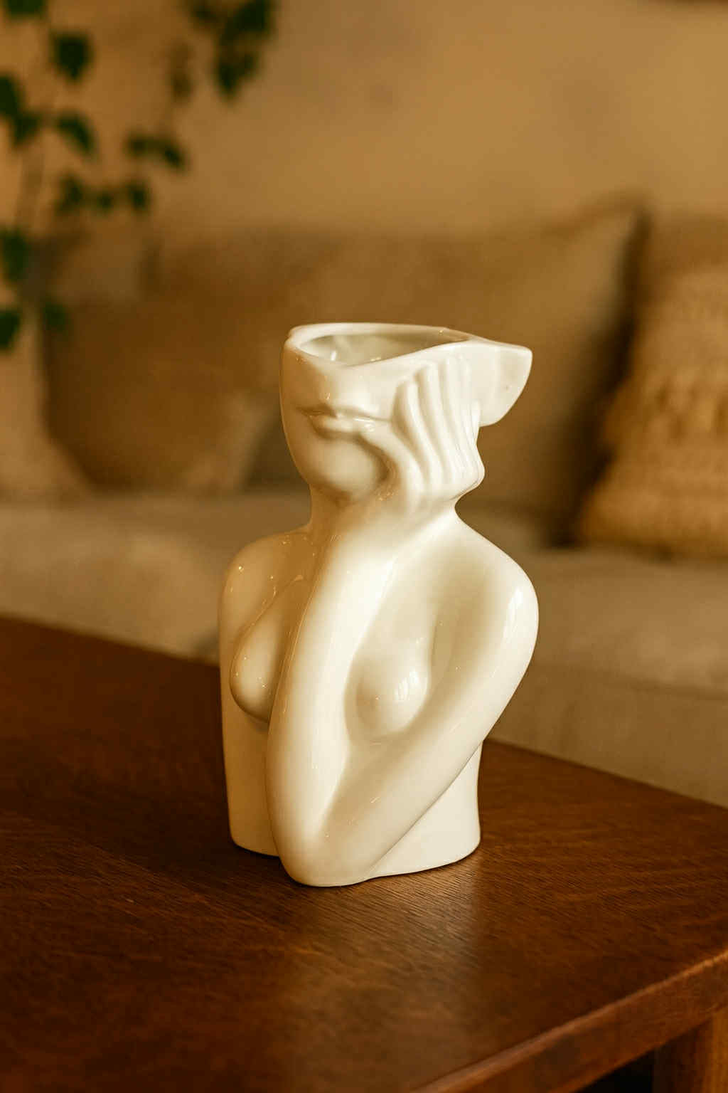 Ceramic sculpture of a nude figure on a wooden table with a blurred sofa in the background