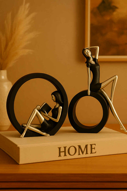 Decorative figurines of a woman reading a book and a man on a bicycle on a 'HOME' book.