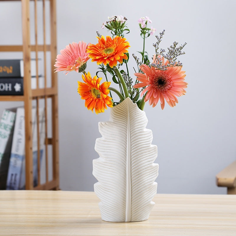 White leaf-shaped vase with colorful flowers on a wooden surface