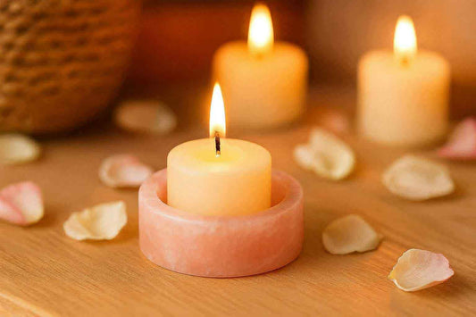 Candle in a pink holder with other candles and petals on a wooden surface