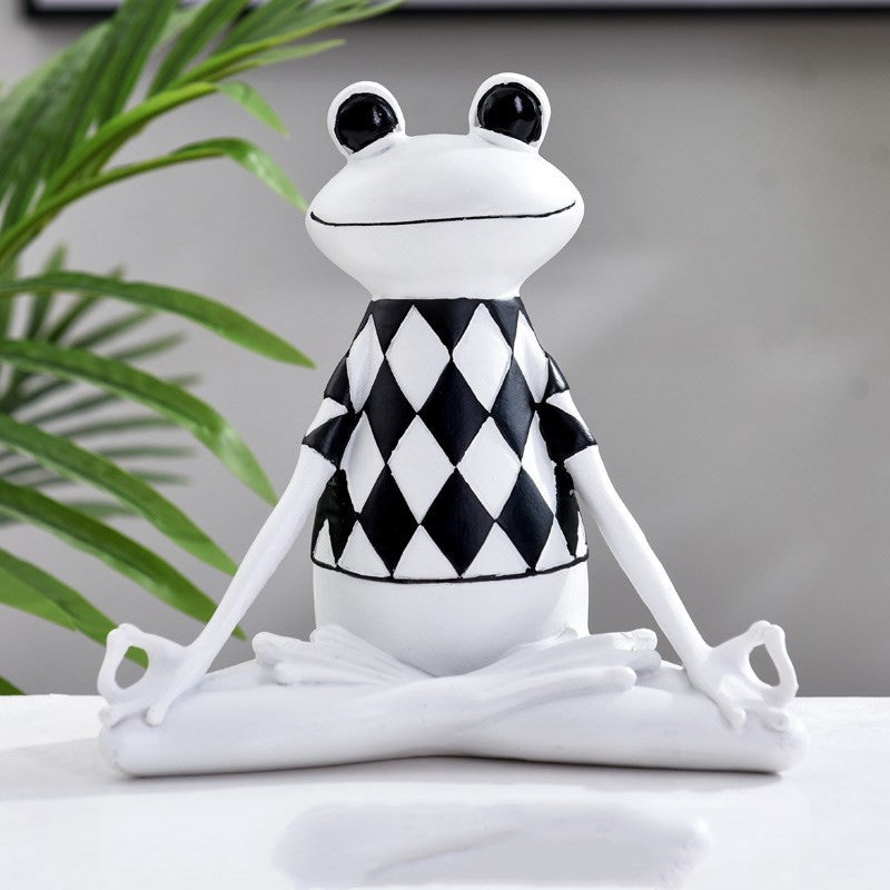 White frog figurine wearing a black and white checkered sweater on a gray background