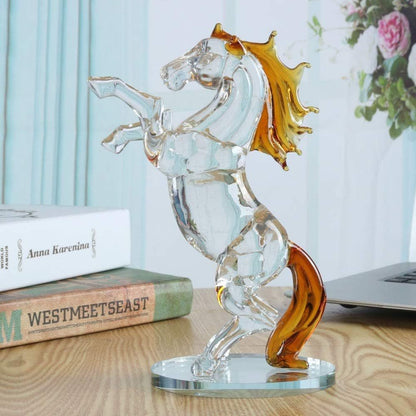 Glass sculpture of a winged figure with amber accents on a wooden surface.