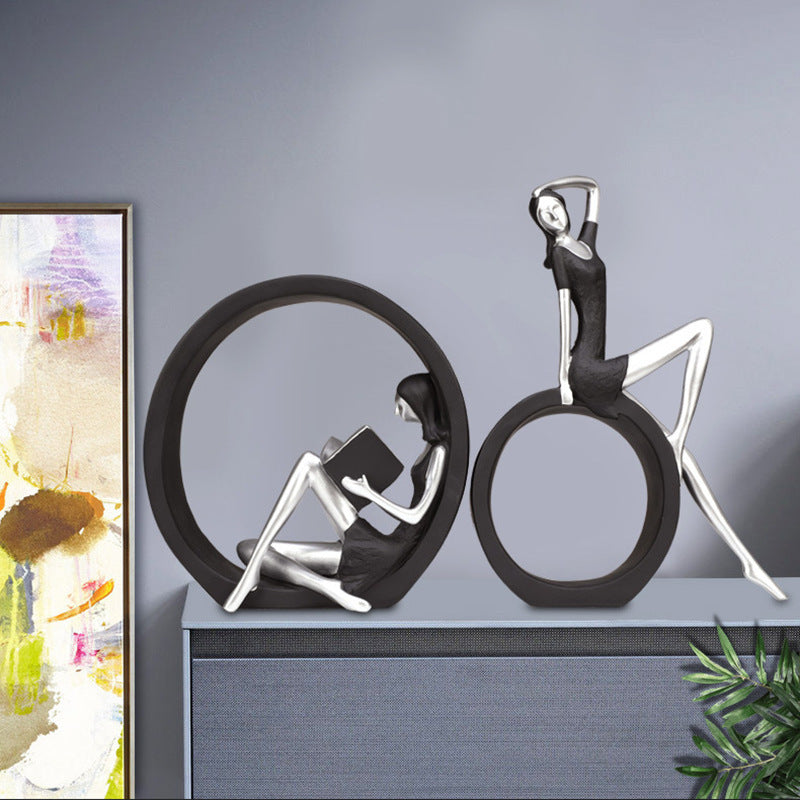 Decorative sculpture of two people in a circle on a shelf with a painting in the background.