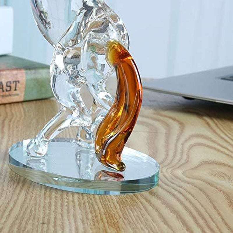 Clear glass figurine of a cat with an amber-colored tail on a wooden surface.
