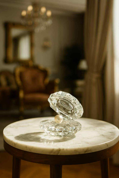 Glass sculpture of an oyster with a pearl on a marble surface in a room with furniture and decor.