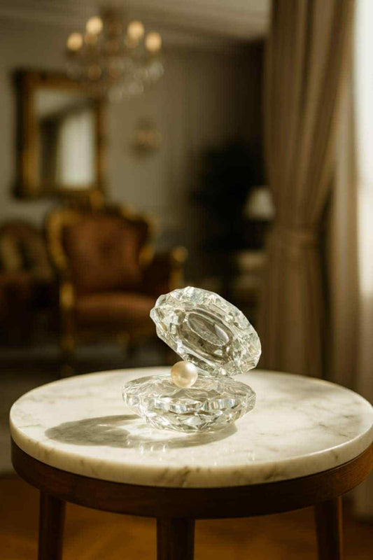 Glass sculpture of an oyster with a pearl on a marble surface in a room with furniture and decor.