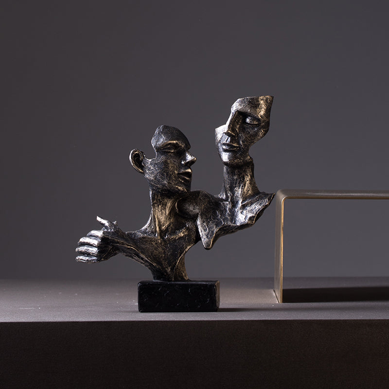 Bronze sculpture of two abstract figures on a dark surface with a gray background
