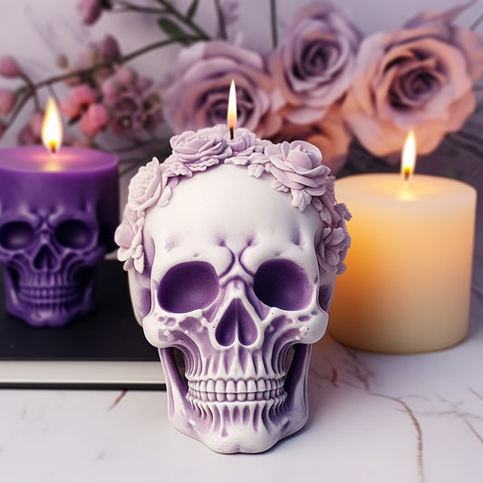 Purple skull-shaped candle with floral details surrounded by other candles and flowers on a marble surface.