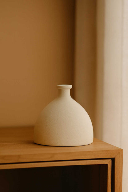 White ceramic vase on a wooden shelf against a beige wall